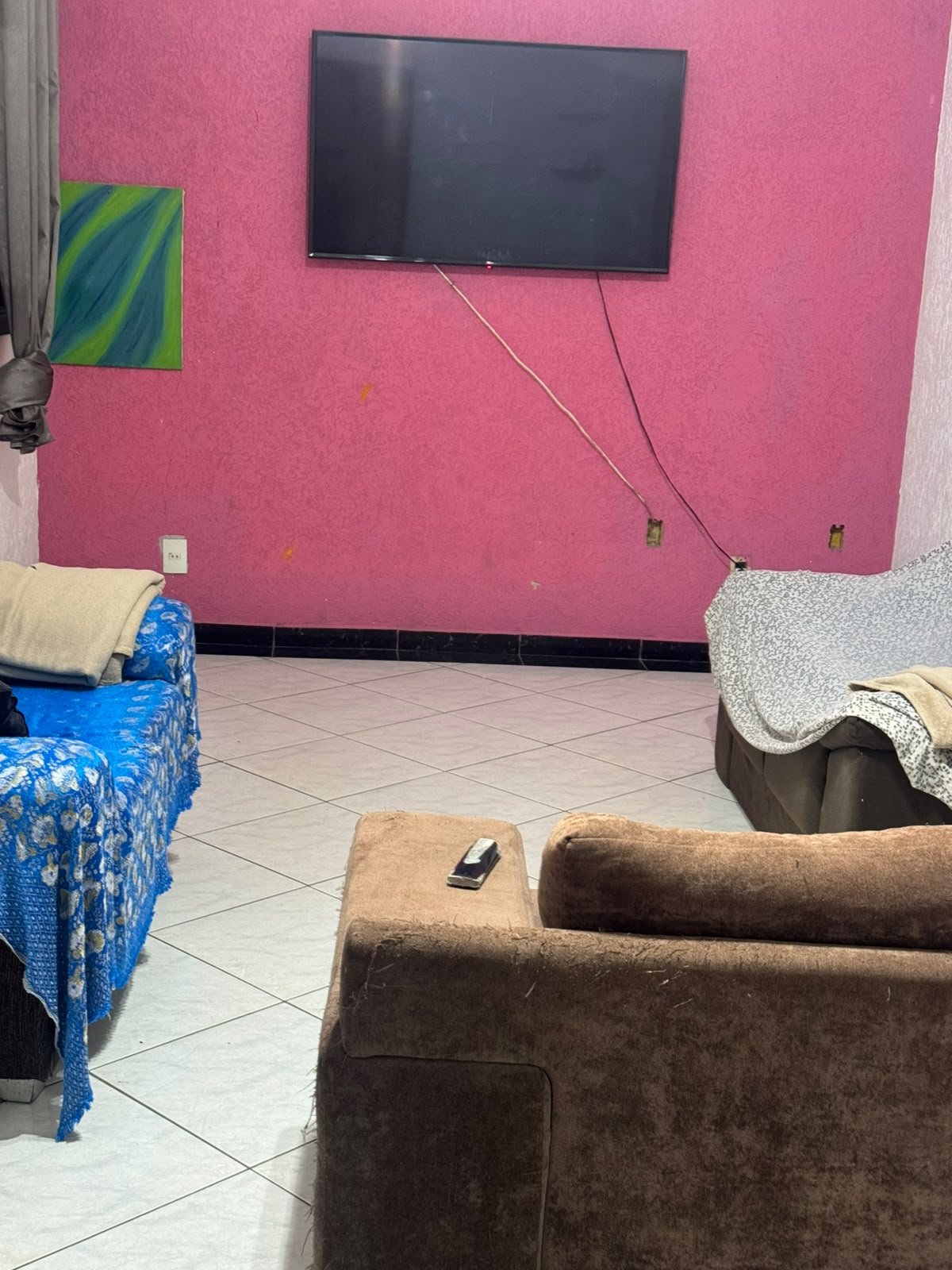 Sala de estar com TV na parede rosa, sofá azul e sofá marrom