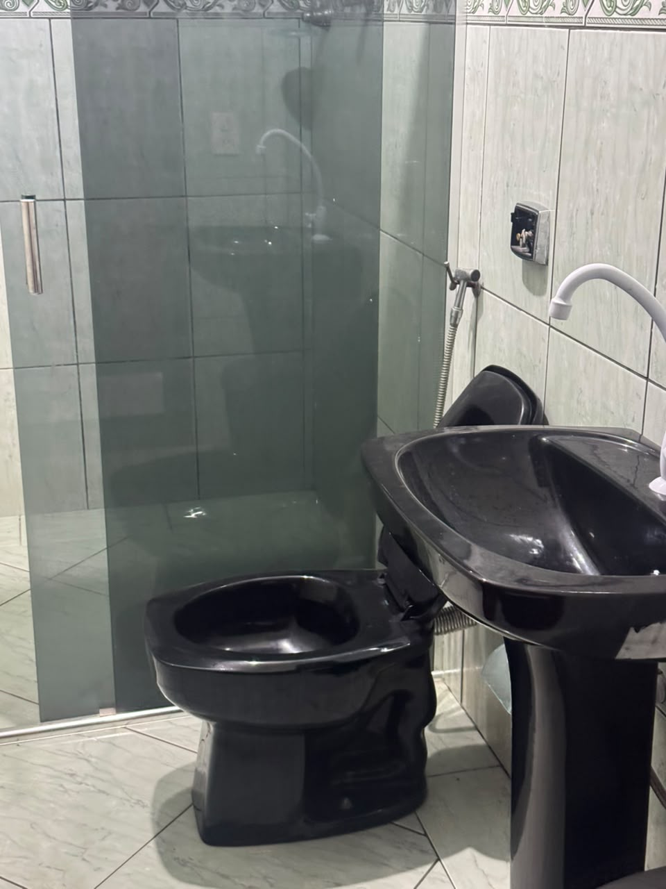 Banheiro com vaso e lavatório pretos e box de vidro com chuveiro