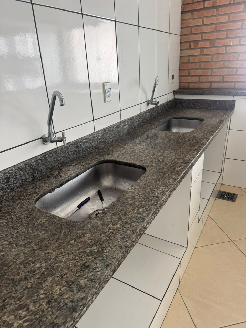 Bancada longa de granito com duas pias de inox na cozinha