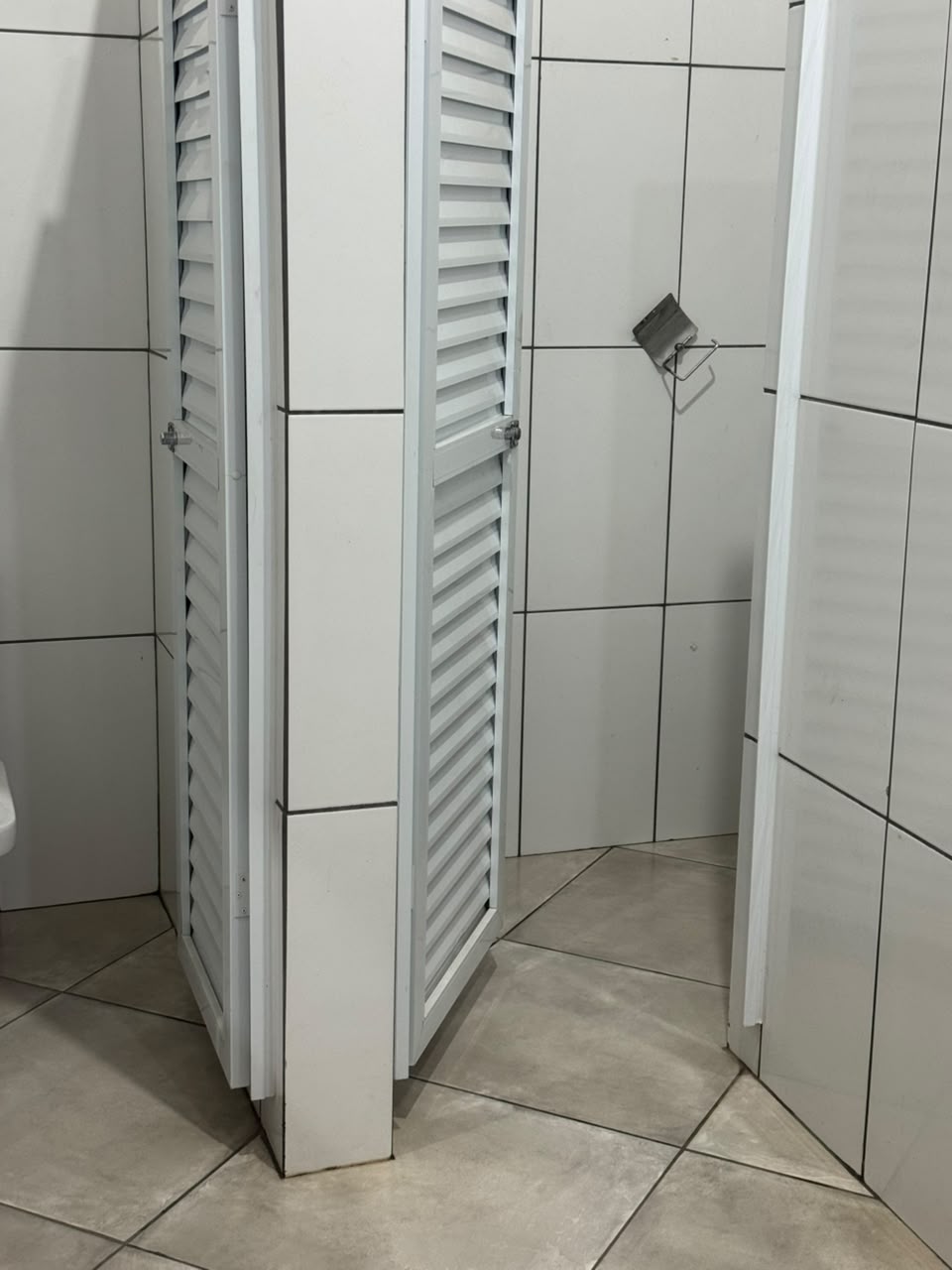 Cabines de banheiro com portas brancas de veneziana e azulejos claros